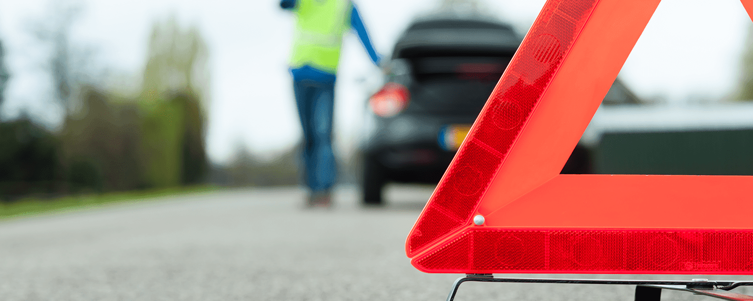 Breakdown insurance: Red triangle warning propped up near a person standing outside of their car.