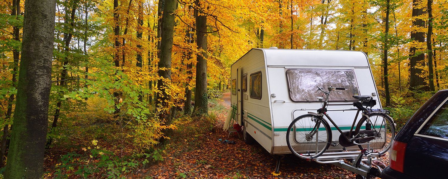 Caravan insurance: A caravan sitting in the woods attached to a car with a bike holder.