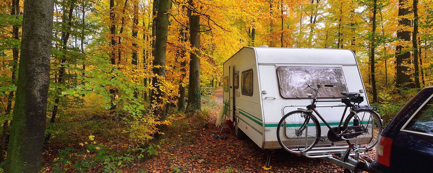 Caravan insurance: A caravan sitting in the woods attached to a car with a bike holder.