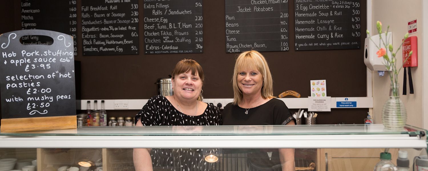 Retailers insurance: Two smiling women standing together behind a cafe counter.
