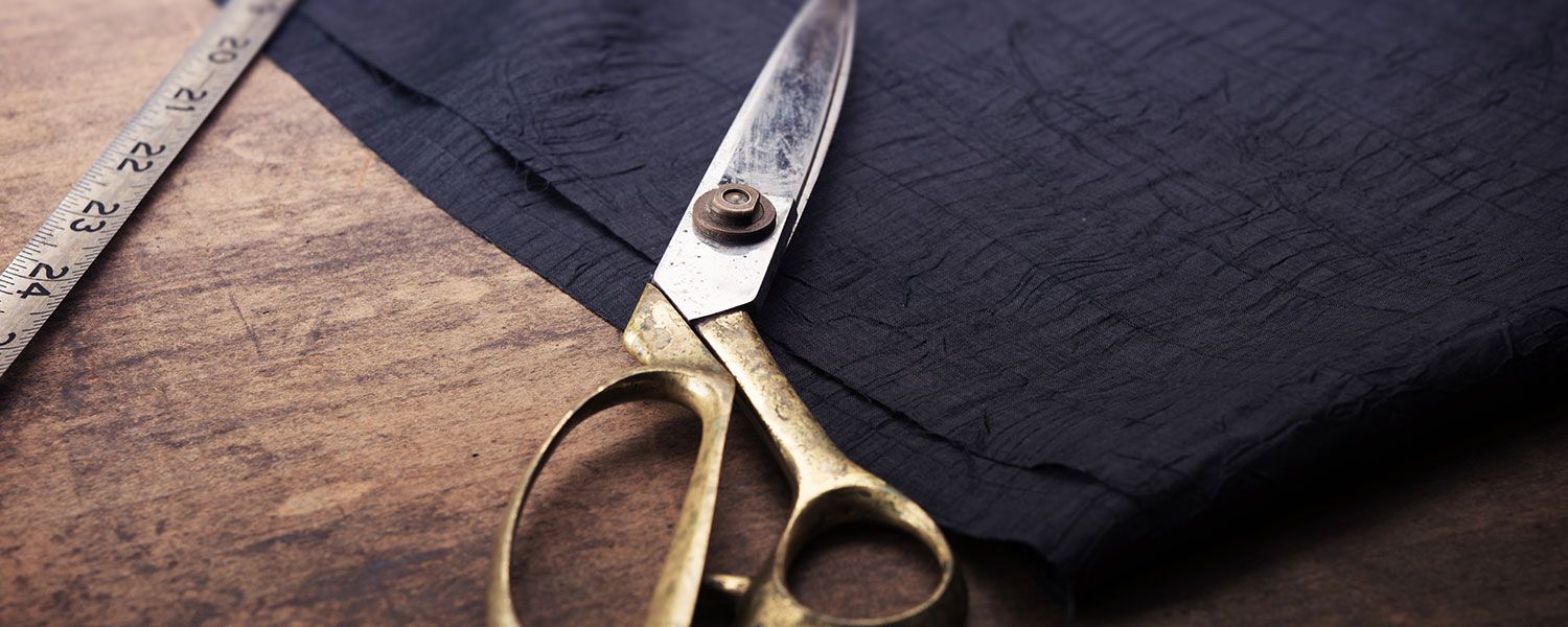 Tailor shop insurance: A pair of scissors lying on a piece of fabric next to a tape measure. 
