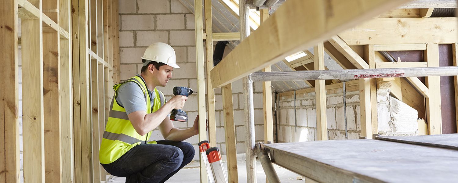 Tradespeople insurance: A male builder using a drill on some wooden planks.
