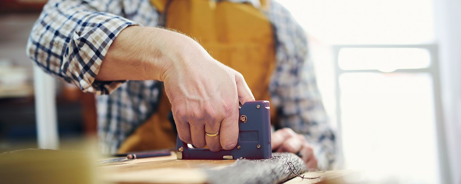 Upholsterers insurance: A woman stapling a peice of fabric to the back of furniture.