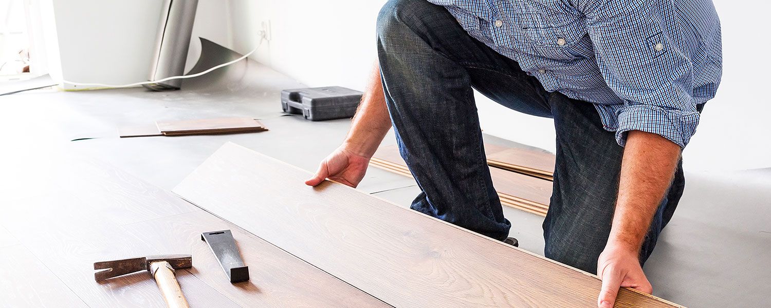 Flooring contractors insurance: A man laying wooden panels on the floor.